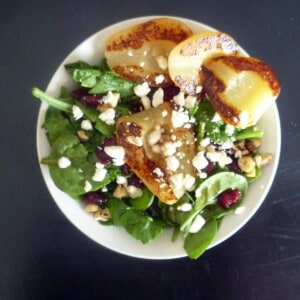 a bed of lettuce in a white bowl topped with feta cheese, dried cranberries, chicken and grilled pears.