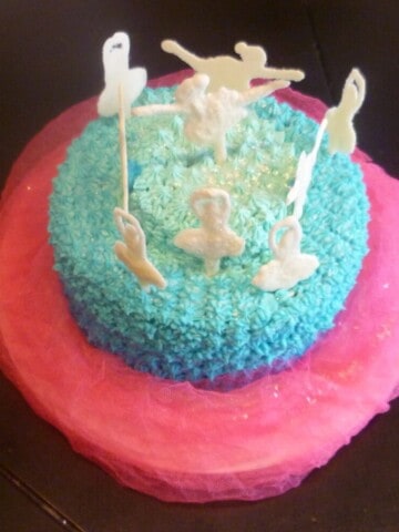 white chocolate ballerina cake. a pink and blue cake is topped with white chocolate ballerinas topped with edible glitter.