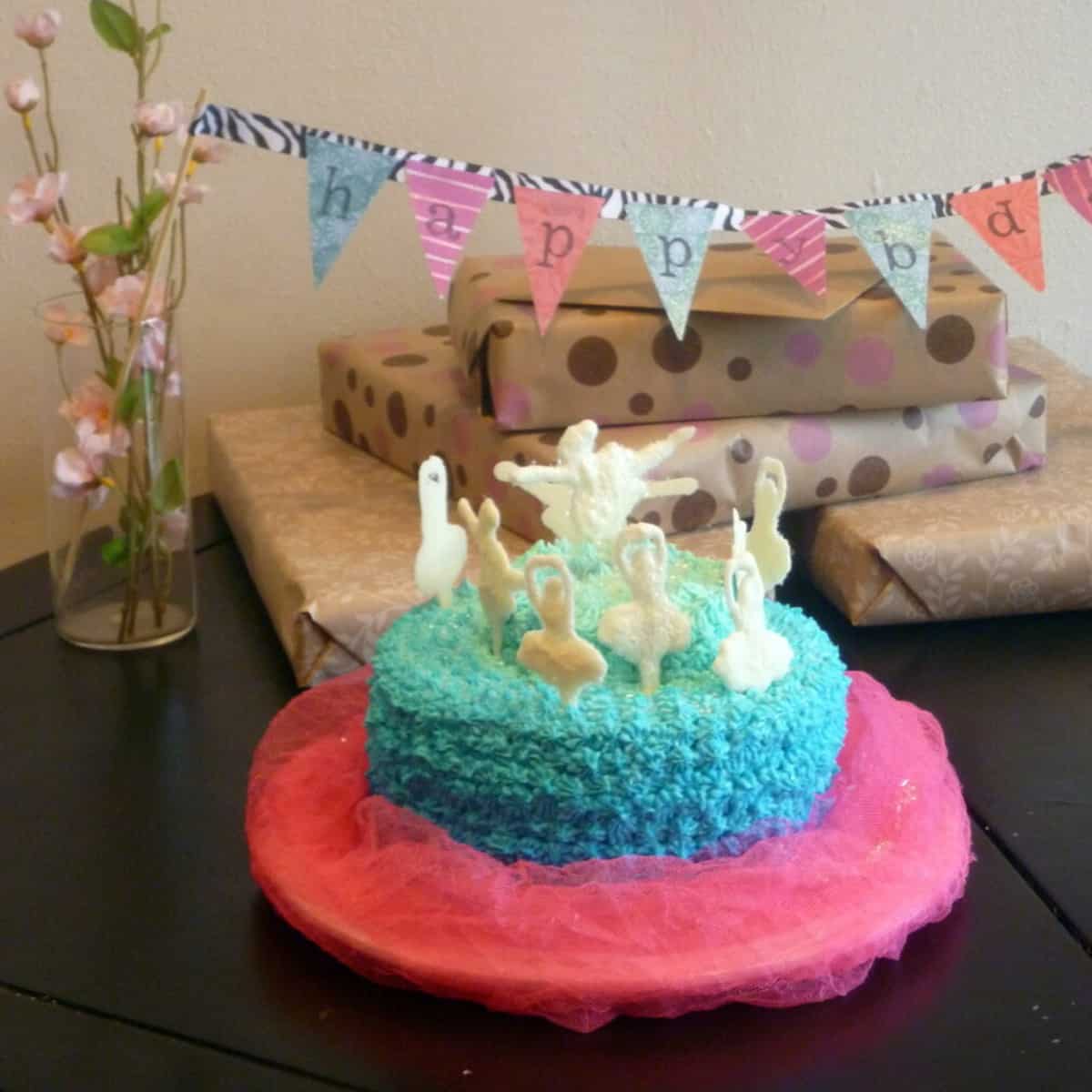 a picture of a ballerina cake with edible glitter on top. The cake is surrounded by a happy birthday banner and presents. 