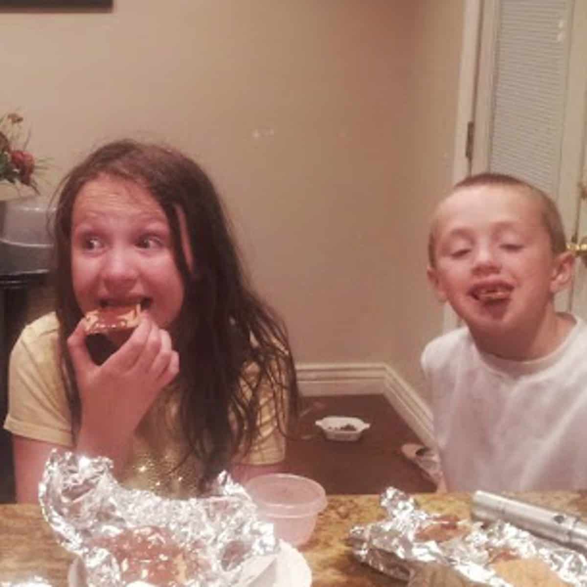 two children enjoying a tin foil smores dessert. the children have chocolate and marshmallow all over their faces and fingers
