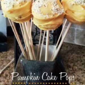 Close-up of a vase filled with pumpkin cake pops. The cake pops are decorated with orange frosting and sprinkles, and they have a green stem