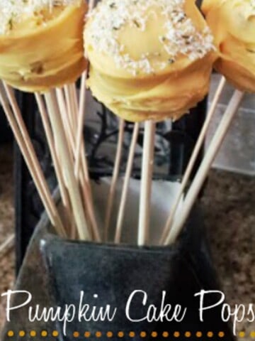Close-up of a vase filled with pumpkin cake pops. The cake pops are decorated with orange frosting and sprinkles, and they have a green stem