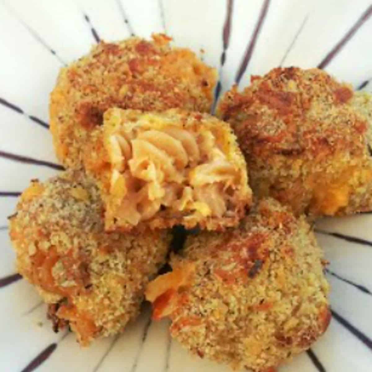 A plate of baked macaroni and cheese balls on a table. The macaroni and cheese balls are golden brown and crispy on the outside, and cheesy and gooey on the inside. The macaroni and cheese balls are served with a side of marinara sauce for dipping.