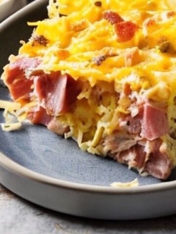 A slice of crockpot breakfast casserole on a white plate. The casserole is made with hash browns, ham, cheese, and eggs.