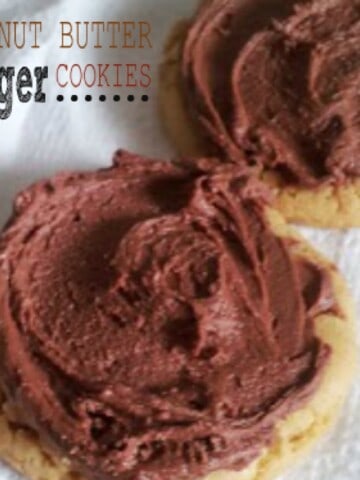 Two peanut butter finger cookies on a white plate. The cookies are round and slightly golden brown. They are topped with chocolate frosting