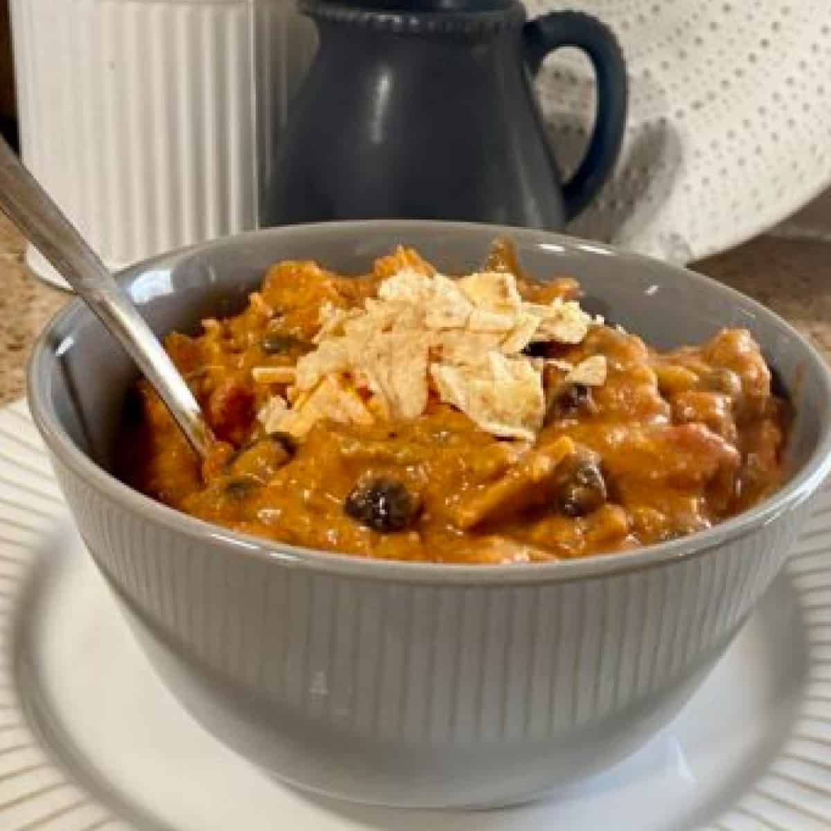 A heaping bowl of Zupa's chicken enchilada chili, brimming with tender chicken, flavorful enchilada sauce, and a medley of chili beans, vegetables, and spices. the chili is topped with cheese