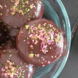 A glass bowl filled with chocolate covered cookies. The chocolate glaze on the cookies is smooth and shiny, and it has hardened to a hard shell.
