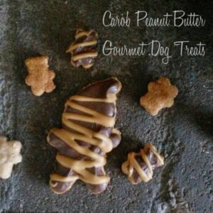 A pile of peanut butter carob dog treats on a table. The treats are shaped like bones, hearts, and stars, and they are topped with peanut butter chips and carob drizzle.