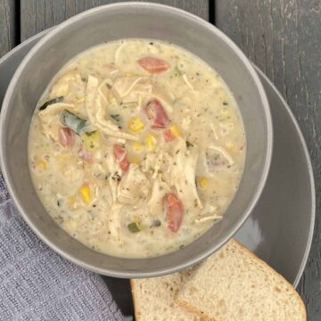 a gray bowl of Zupas garden chowder filled with fresh herbs, cheese, cream, zucchini, tomatoes and corn.