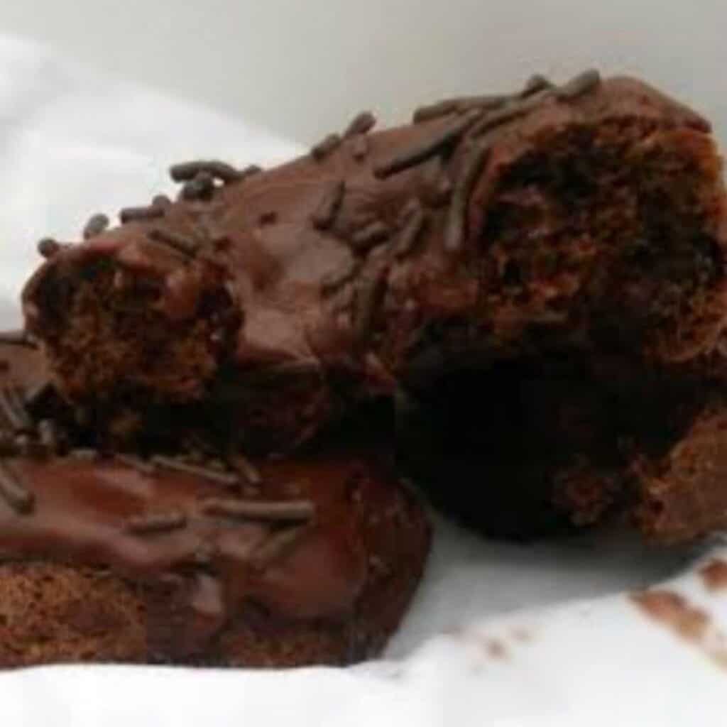 a picture of a brown chocolate donut with an inside view of the chocolate. The donut is topped iwth brown chocolate forsting and topped with chocolate sprinkles. 