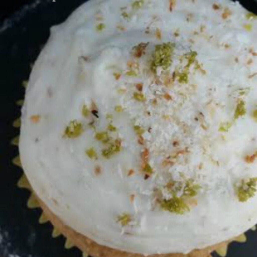 a picture of coconut pineapple lime cupcakes. an overhead view of the cupcake topped with lime zest and toasted coconut is featured. 