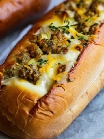 a photo of a french baguette with the center cut and hollowed out. Inside is a cheese and sausage mixture with cream cheese, onions, parsley, cheddar and swiss cheese.