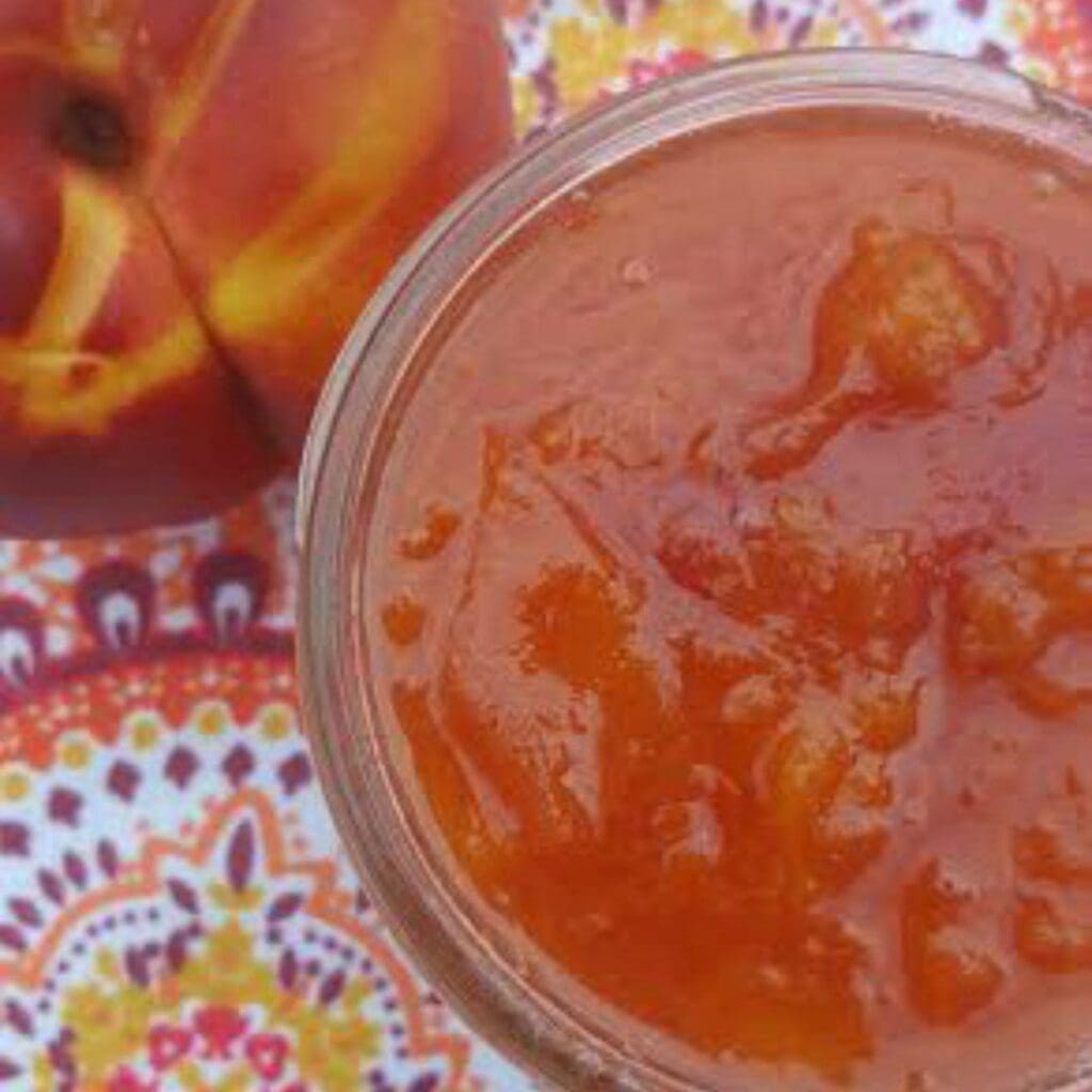 a photo of orange nectarine jam in a mason jar. the jam is bright and there are some small pieces of nectarine.