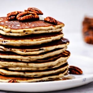 A close-up photo of a plate of Candied Pecan Pancakes. The pancakes are fluffy and golden brown, with a generous sprinkling of candied pecans on top. The candied pecans are caramelized and crunchy, adding a touch of sweetness and texture to the pancakes. A drizzle of maple syrup flows over the pancakes, completing the look of this decadent breakfast treat.