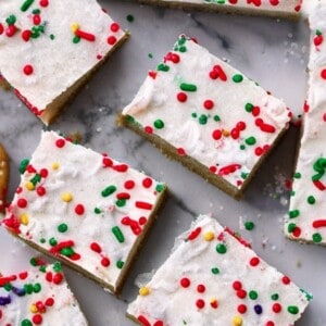 A close-up shot of freshly baked Christmas sugar cookie bars, dusted with powdered sugar and adorned with festive sprinkles.