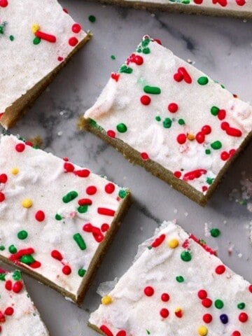 A close-up shot of freshly baked Christmas sugar cookie bars, dusted with powdered sugar and adorned with festive sprinkles.
