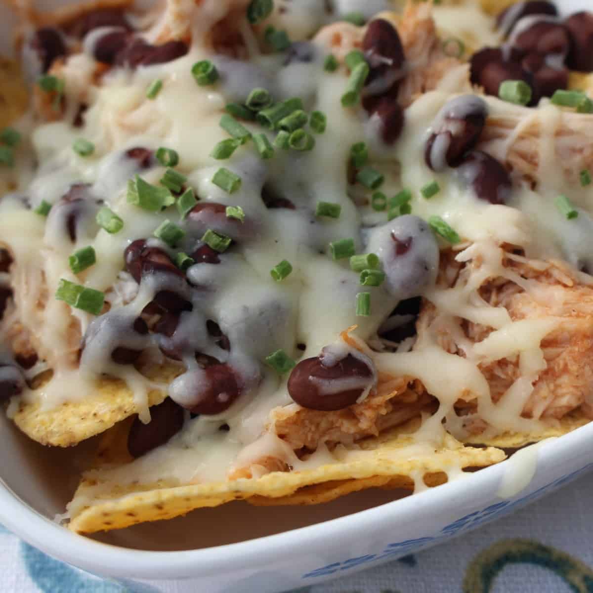 a delicious recipe for bbq chicken nachos with melted cheese, barbeque chicken and toppings like beans, chives and bacon
