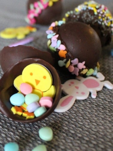 A photorealistic image of a half-opened Kinder Surprise egg, revealing a smooth milk chocolate exterior and a colorful plastic capsule filled with a yellow toy.