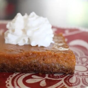 A slice of sheet pan pumpkin pie with a graham cracker gingersnap crust and a dollop of whipped cream on top.