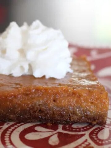 A slice of sheet pan pumpkin pie with a graham cracker gingersnap crust and a dollop of whipped cream on top.