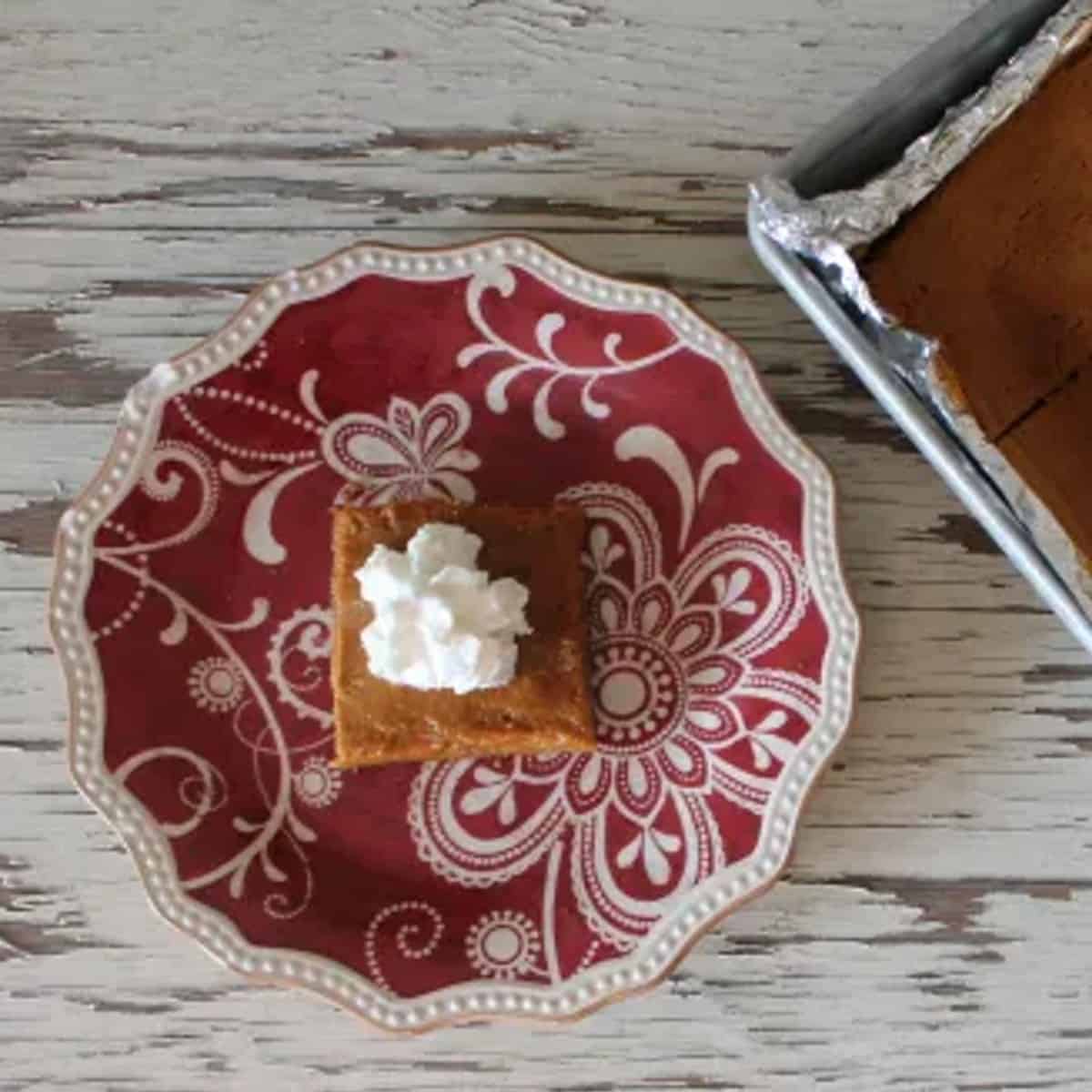 a delicious slice of sheet pan pie crust with a red plate and a square slice of pie with a dollop of whipped cream on top