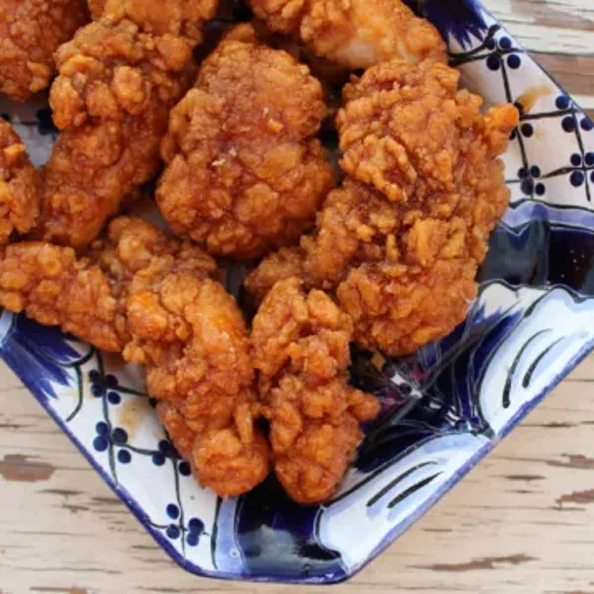 A heaping plate of spicy honey garlic chicken tenders on a blue and white plate. 