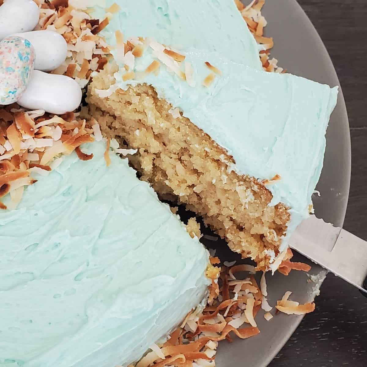 A close-up photo of a slice of easter coconut cake being cut with a fork, revealing the moist cake crumb and fluffy coconut cream frosting.
