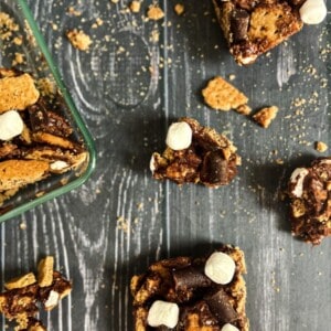 A close-up photo of several rectangular s'mores bars on a brown paper bag. Each Golden Graham cereal bars consists of a graham cracker base, topped with a layer of marshmallow and chocolate. The marshmallows are golden brown and toasted, and the chocolate is melted and hardened