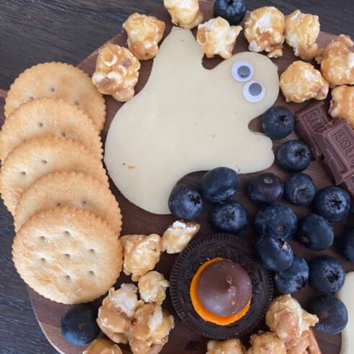 A Halloween charcuterie board arranged with crackers, popcorn, blueberries, cheese ghosts, Oreo witches hats, and caramel popcorn. 