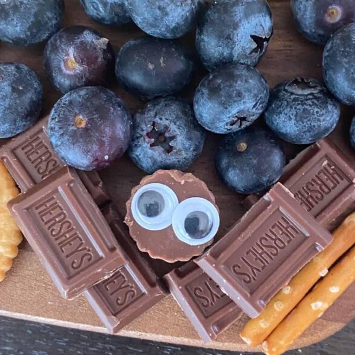 A photo of a Halloween bat made with Hershey's chocolate bars and a Reese's peanut butter cup in the center. The eyes are made with plastic googly eyes. The bat is arranged on a Halloween dessert board.