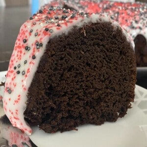 A photo of a stunning black velvet cake on a cake stand. The cake is layered and frosted with a smooth, deep black frosting. The top of the cake is decorated with a cascade of colorful chocolate shavings that resemble dripping blood.
