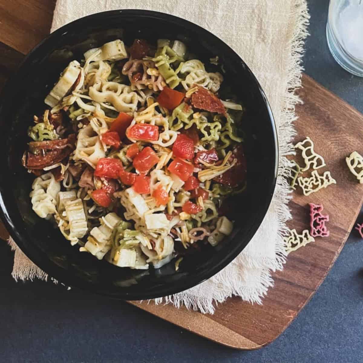 A black bowl filled with colorful alphabet fun pasta shapes on a wooden cutting board