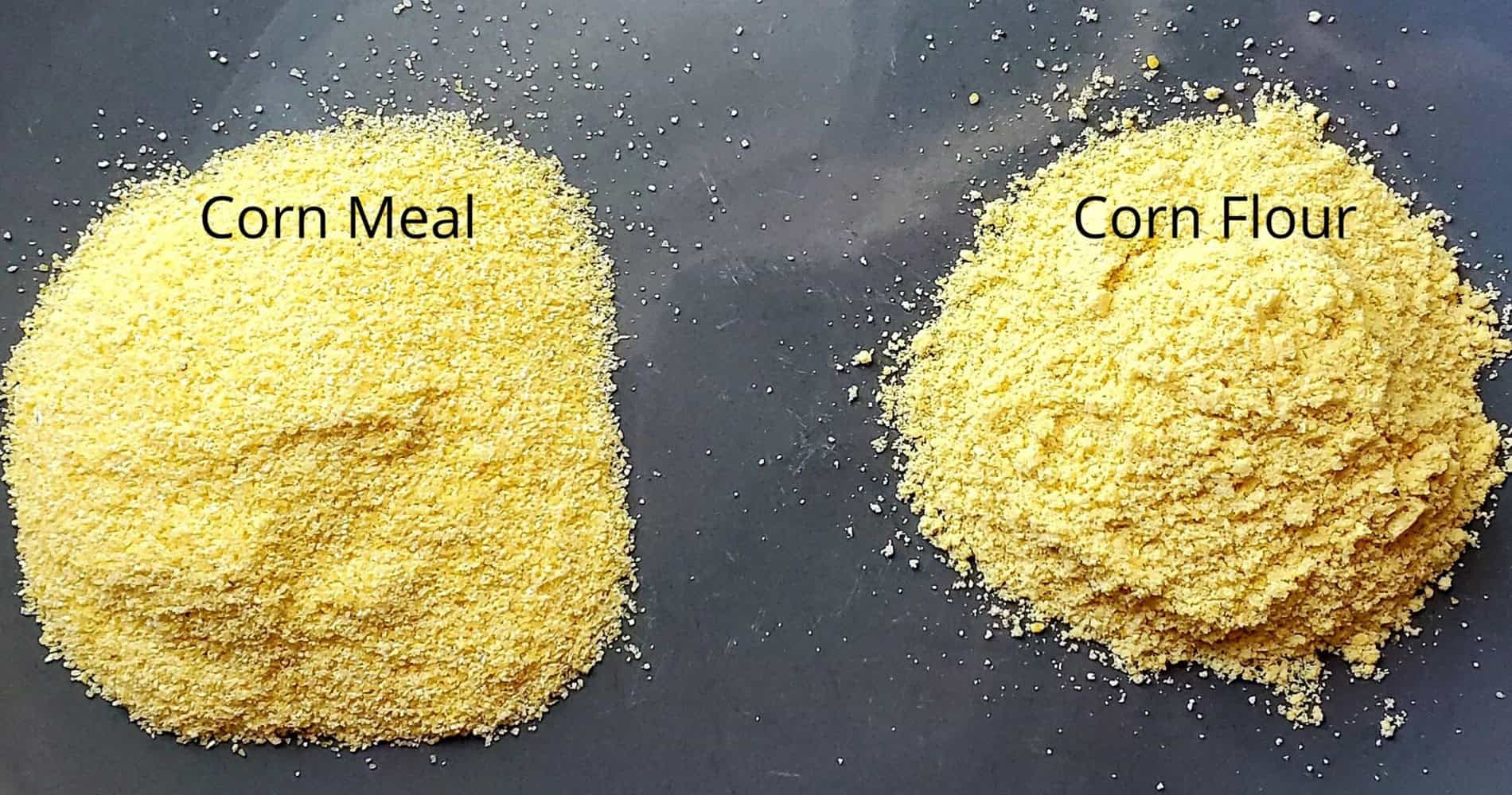 Two piles of cornmeal and corn flour side-by-side on a wooden table. The pile on the left is labeled "Corn Meal" and is coarse with large yellow flakes. The pile on the right is labeled "Corn Flour" and is finer with a lighter yellow color.