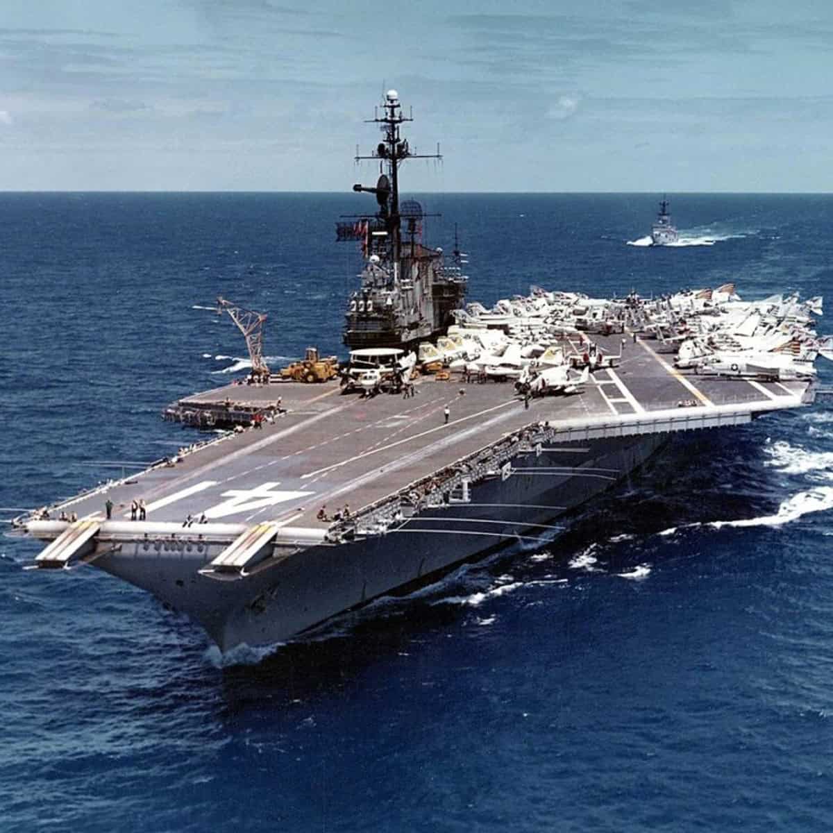 A large military aircraft carrier, the USS Midway, floating on a calm blue ocean. In the distance, a smaller ship is also visible.