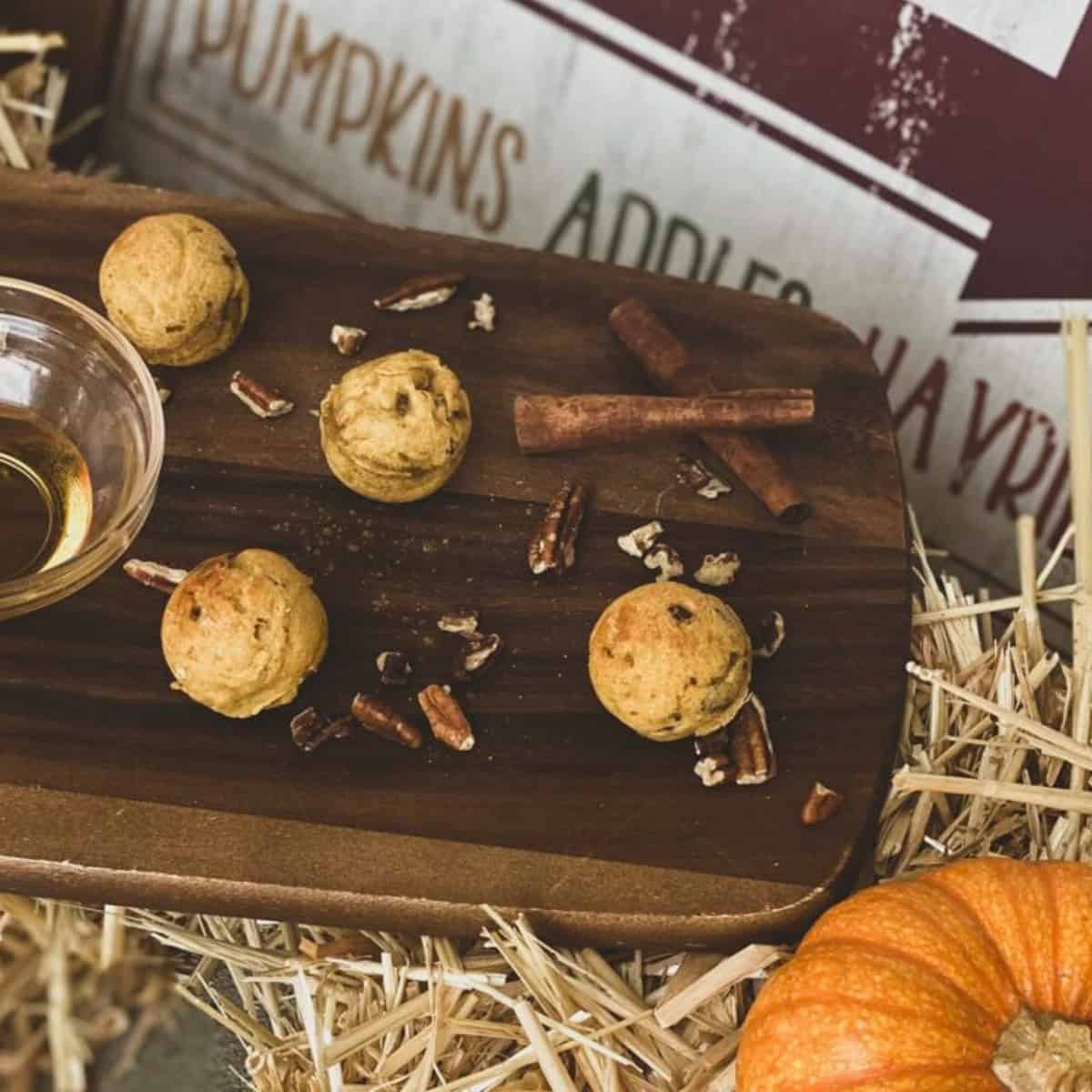 Four mini pumpkin pecan pancake arranged on a wooden board. The pancakes are golden brown and topped with chopped pecans. Cinnamon sticks and additional pecan pieces are scattered around the pancakes.