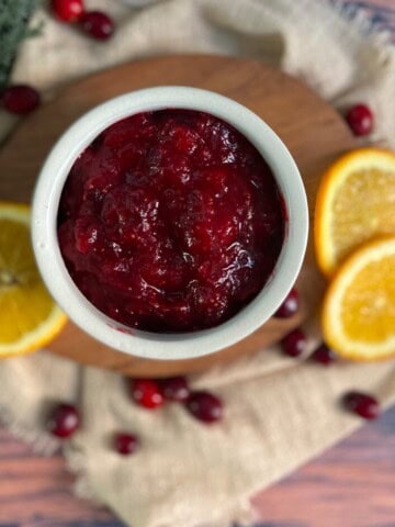 A bowl of whole berry cranberry sauce. The cranberries are a deep red color and appear whole. The sauce is a thick, jelly-like consistency with a glossy sheen.