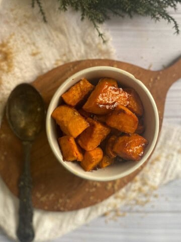 A rectangular white serving platter filled with roasted sliced sweet potatoes. The sweet potato slices are a golden brown color and have crispy edges. Some slices have a sprinkle of a brown sugary substance on top.