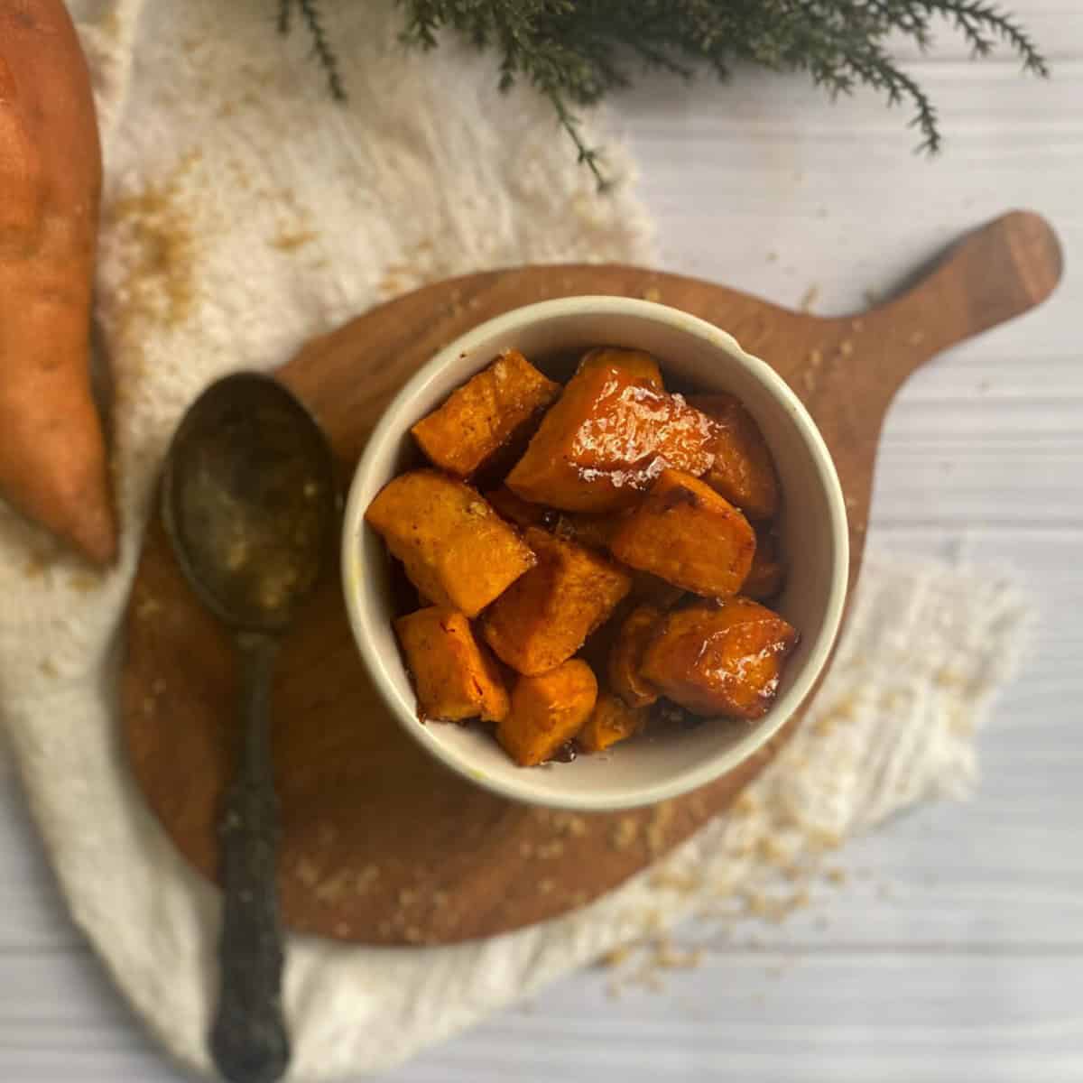 A rectangular white serving platter filled with roasted sliced sweet potatoes. The sweet potato slices are a golden brown color and have crispy edges. Some slices have a sprinkle of a brown sugary substance on top.