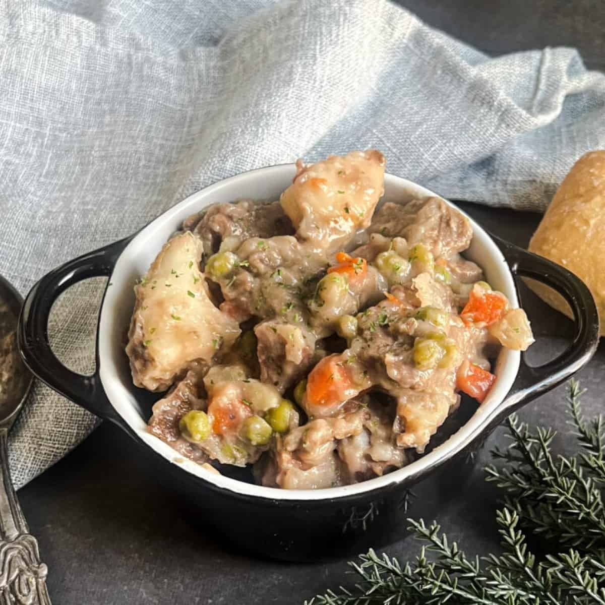 A bowl of beef stew with frozen vegetables, potatoes, carrots, and celery in a thick, brown gravy. The stew is garnished with fresh herbs and served with a side of crusty bread.