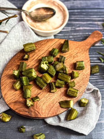 roasted okra fries are on a brown serving board and blue background.