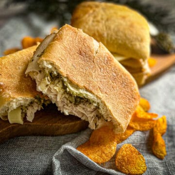 pesto provolone turkey sandwich recipe on a cutting board with barbeque chips and blue background