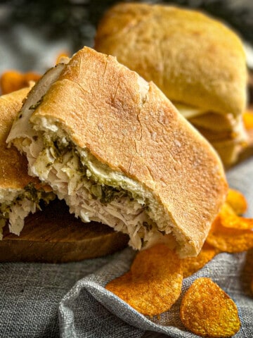 pesto provolone turkey sandwich recipe on a cutting board with barbeque chips and blue background