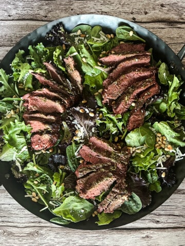 A grilled steak topped with a generous amount of pesto sauce. The steak is cooked to perfection, with a crispy sear on the outside and a tender, juicy interior. The pesto sauce is made with fresh basil, pine nuts, Parmesan cheese, and olive oil. It is a delicious and flavorful combination that is sure to please.
