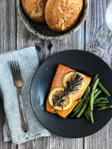 A plate of rosemary lemon salmon with roasted vegetables. The salmon is golden brown and flaky, and the vegetables are tender and caramelized. The dish is garnished with fresh herbs.