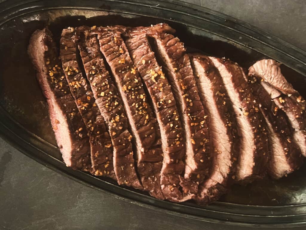 a beautiful london broil steak with a rub on it and sliced on a platter. 