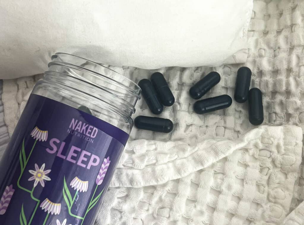 a photo of a pillow and blanket is shown in the picture. A purple pill bottle with the words Naked Nutrition are on them. Several purple pill capsules lie beside the bottle. 