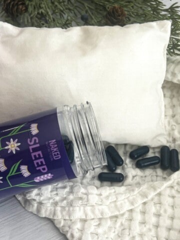A close-up of a bottle of sleep aid supplements sitting on top of a white pillow. The bottle has a white label with the word "sleep" in blue letters. The bottle also has a blue cap.