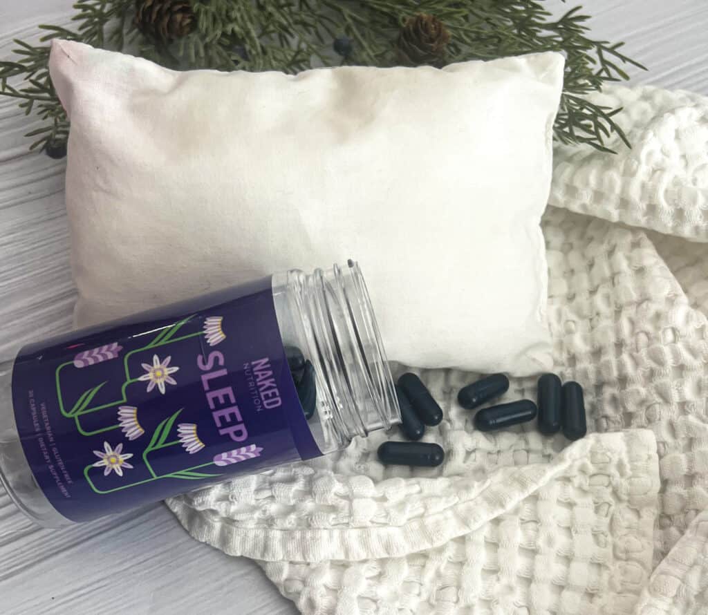 a picture of naked nutrition natural sleep supplement. A picture of a pillow and blanket are shown. A bottle with flowers is shown. There are purple pill capsules shown in the photo. 