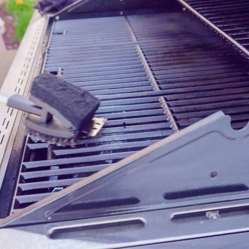 a wire brush is being used to clean and prepare a gas grill for smoking meats. 