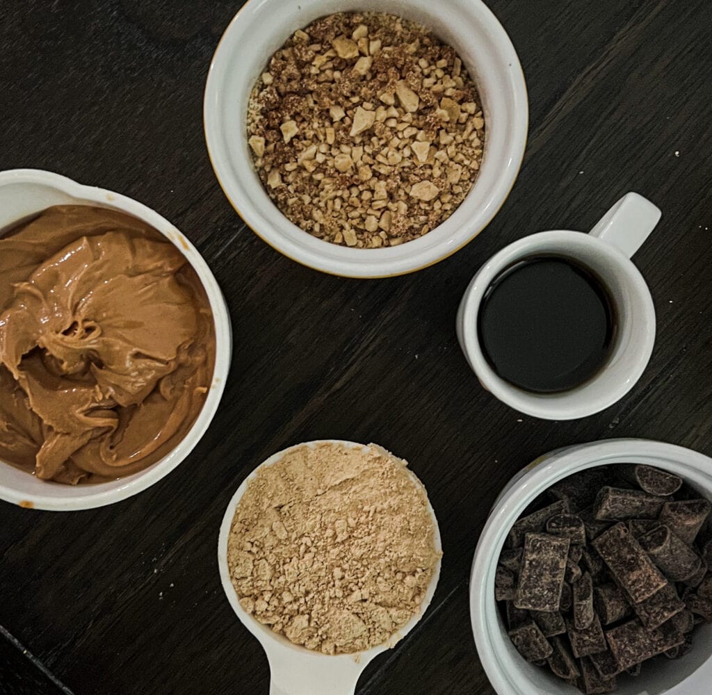 a photo of ingredients needed for peanut butter protein powder bars. Pictured are chocolate chips, graham cracker crumbs, maple syrup and honey, peanut butter and peanut butter protein powder. 